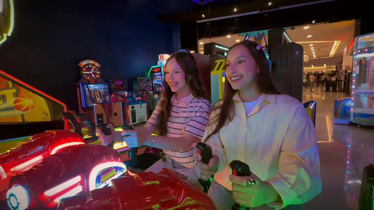 Duas amigas rindo no simulador de corrida, com a área de jogos acesa ao fundo