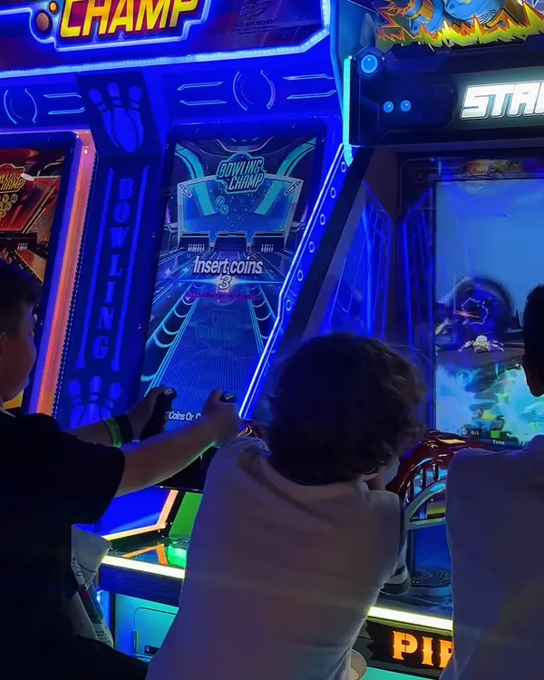 Crianças de costas jogando lado a lado nas máquinas iluminadas